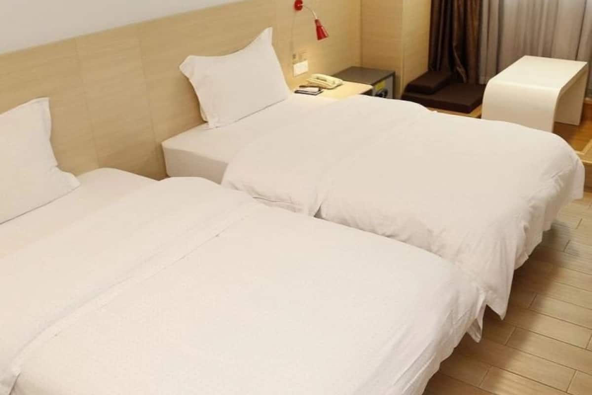 Une chambre d’hôtel avec deux lits, une table de chevet avec une lampe, une chaise et une fenêtre avec des rideaux.