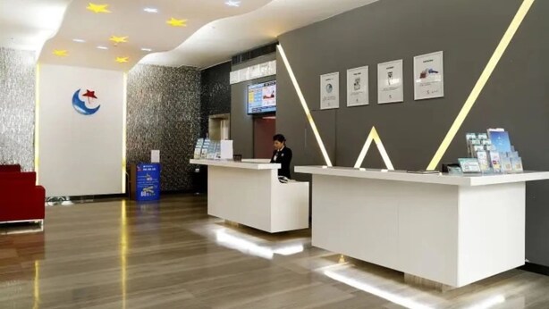 Een moderne receptiebalie met een receptioniste, een digitaal scherm en een logo op de muur.