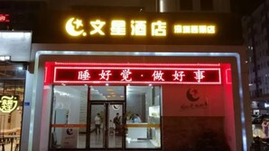Een hotel met een opvallend bord in Chinese karakters, een rode neonreclame boven de ingang en een zichtbaar interieur met een receptiebalie.
