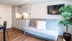 A modern living room with a grey sofa, a flat-screen TV mounted on the wall, a dining table with chairs, and a potted plant. - ZH Schmidgasse I - Hitrental Apartment (Zürich)