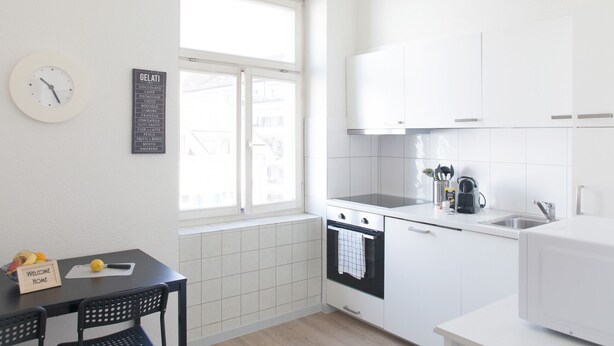 A modern kitchen with white cabinets, a black countertop, and a window with a view of buildings. - ZH Seefeld - Hitrental Apartment (Zürich)