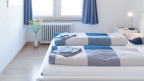 A bedroom with a bed, a bedside table, a lamp, a window with curtains, and a radiator. - ZH Seefeld - Hitrental Apartment (Zürich)