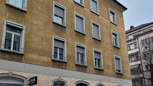 A multi-story building with a textured facade, multiple windows, and a ground-level entrance with a sign. - ZH Seefeld - Hitrental Apartment (Zürich)