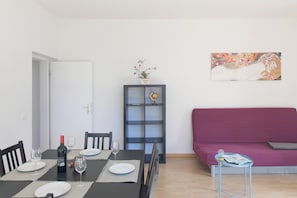 Uma sala de jantar com uma mesa posta para dois, uma garrafa de vinho e um vaso com flores.