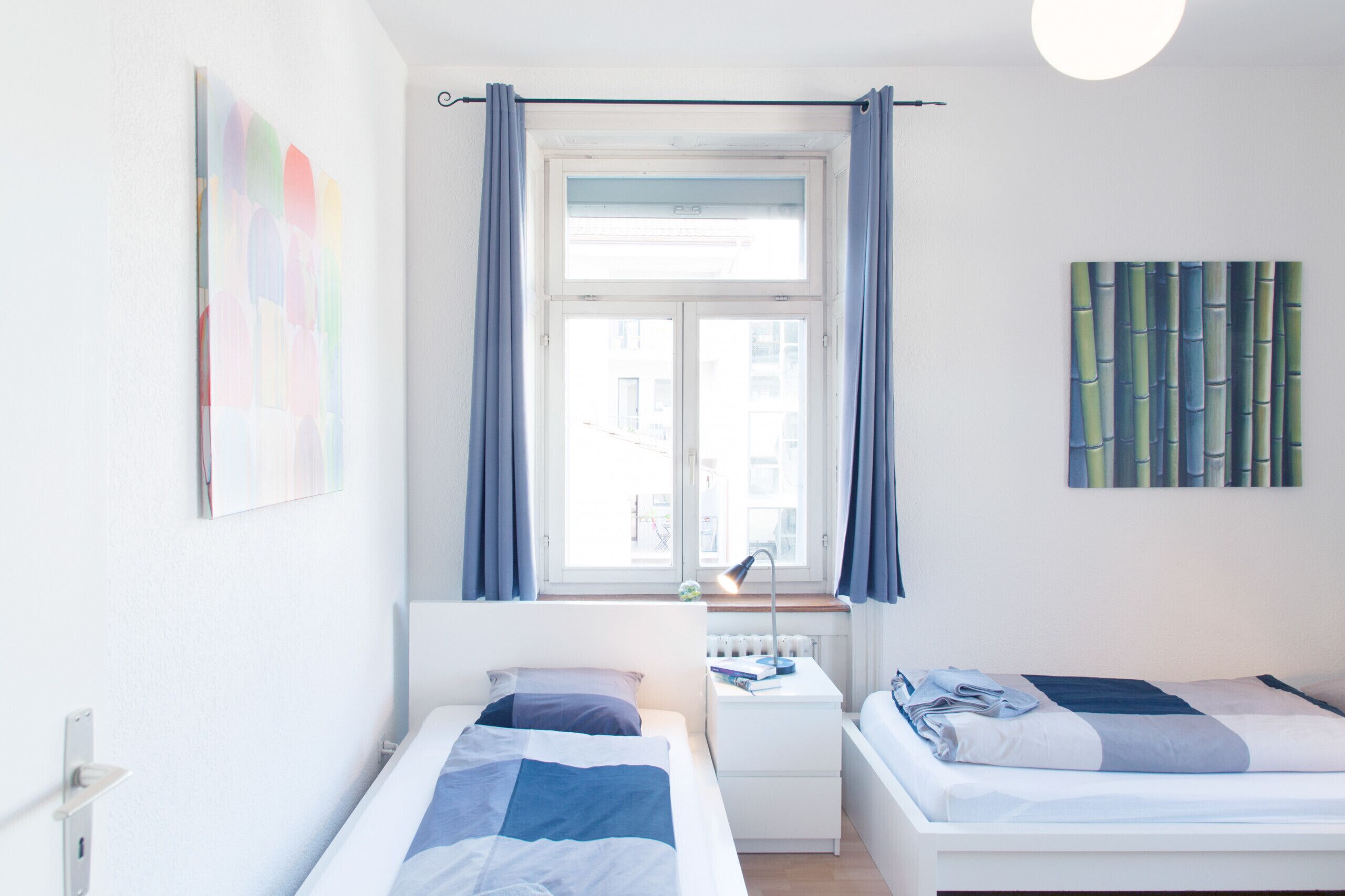 Quarto de hotel moderno com duas camas, uma janela com cortinas, um radiador e uma parede com padrão de bambu.