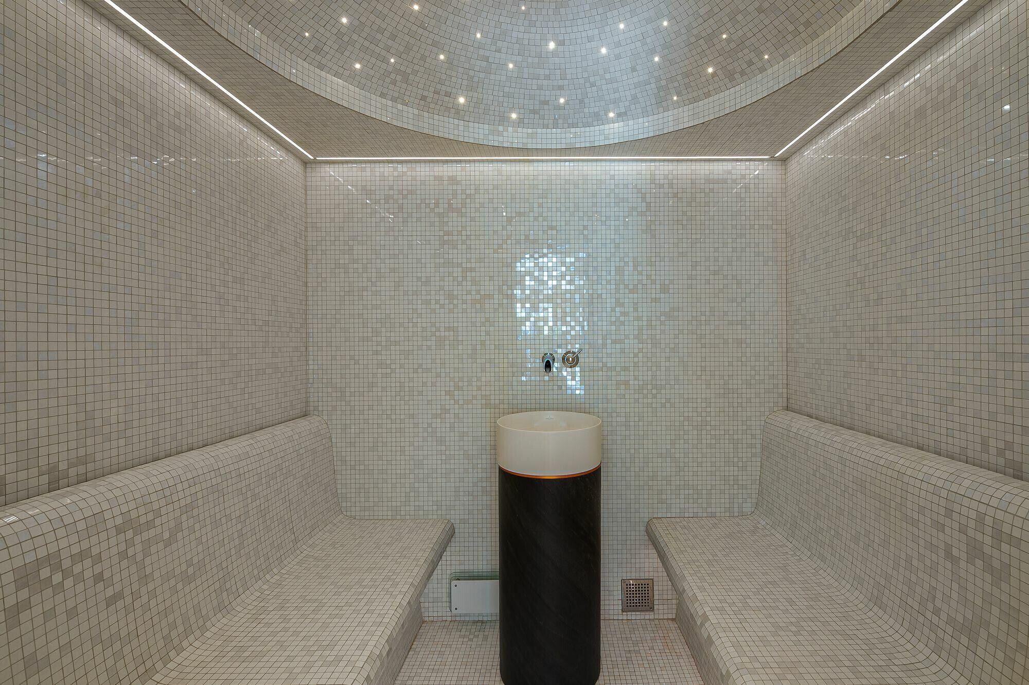 A modern bathroom with a tiled floor and walls, a central sink, and a shower area.