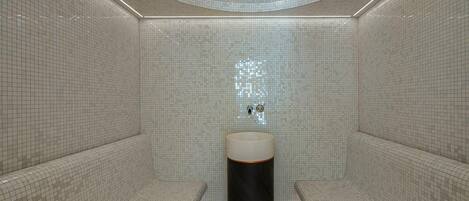 A modern bathroom with a tiled floor and walls, a central sink, and a shower area.