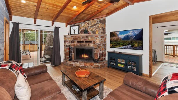Una sala de estar acogedora con chimenea de piedra, sofás de cuero, una mesa de centro de madera y un televisor montado en la pared.