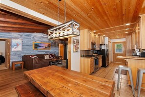 A spacious living area with a wooden dining table, a sofa, and a kitchen with wooden cabinets and a central island.