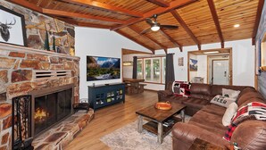 Una sala de estar acogedora con chimenea de piedra, techo de madera y un televisor grande.