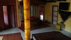 Une pièce avec une grande colonne jaune, un tapis à motifs et une chaise traditionnelle en osier.