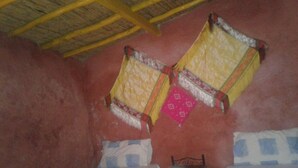 Une pièce avec deux lits, une petite chaise en métal et un plafond recouvert de chaume.