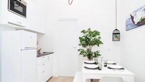A compact kitchen with a built-in oven, a white refrigerator, and a dining area with a table set for two. - Orti - Modern Apartment Porta Romana (Milan)