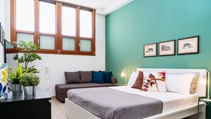 A modern bedroom with a bed, a sofa, a desk with plants, and a window with wooden frames. - Orti - Modern Apartment Porta Romana (Milan)