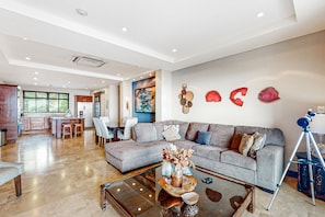 A modern living room with a grey sofa, a coffee table with decorative items, and a telescope on a tripod. - Beautiful condo w/breathtaking ocean & mountain views and shared pool (Playa Ocotal)