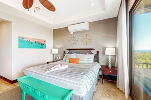 A bedroom with a bed, bedside tables, a view through a large window, and a painting on the wall. - Beautiful condo w/breathtaking ocean & mountain views and shared pool (Playa Ocotal)