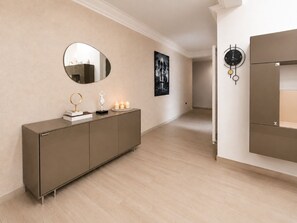 Un couloir avec un mur recouvert de miroirs, un miroir rond, un tableau encadré, une horloge murale et un meuble.