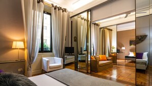 A modern hotel room with a large bed, a sofa, a TV, and a glass partition. - Guercino - Apartment Porta Garibaldi (Milan)