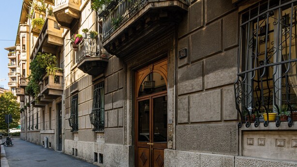 A historic building with a large wooden door, ornate iron balcony railings, and multiple balconies with potted plants. - Guercino - Apartment Porta Garibaldi (Milan)