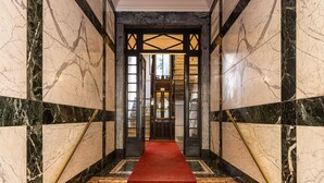 A grand hallway with marble walls, a red carpet, and a staircase leading to a room with a large window. - Guercino - Apartment Porta Garibaldi (Milan)