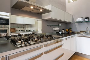 Une cuisine moderne dotée d’une cuisinière en acier inoxydable, de meubles blancs et d’une étagère en verre où sont rangés les appareils de cuisine.