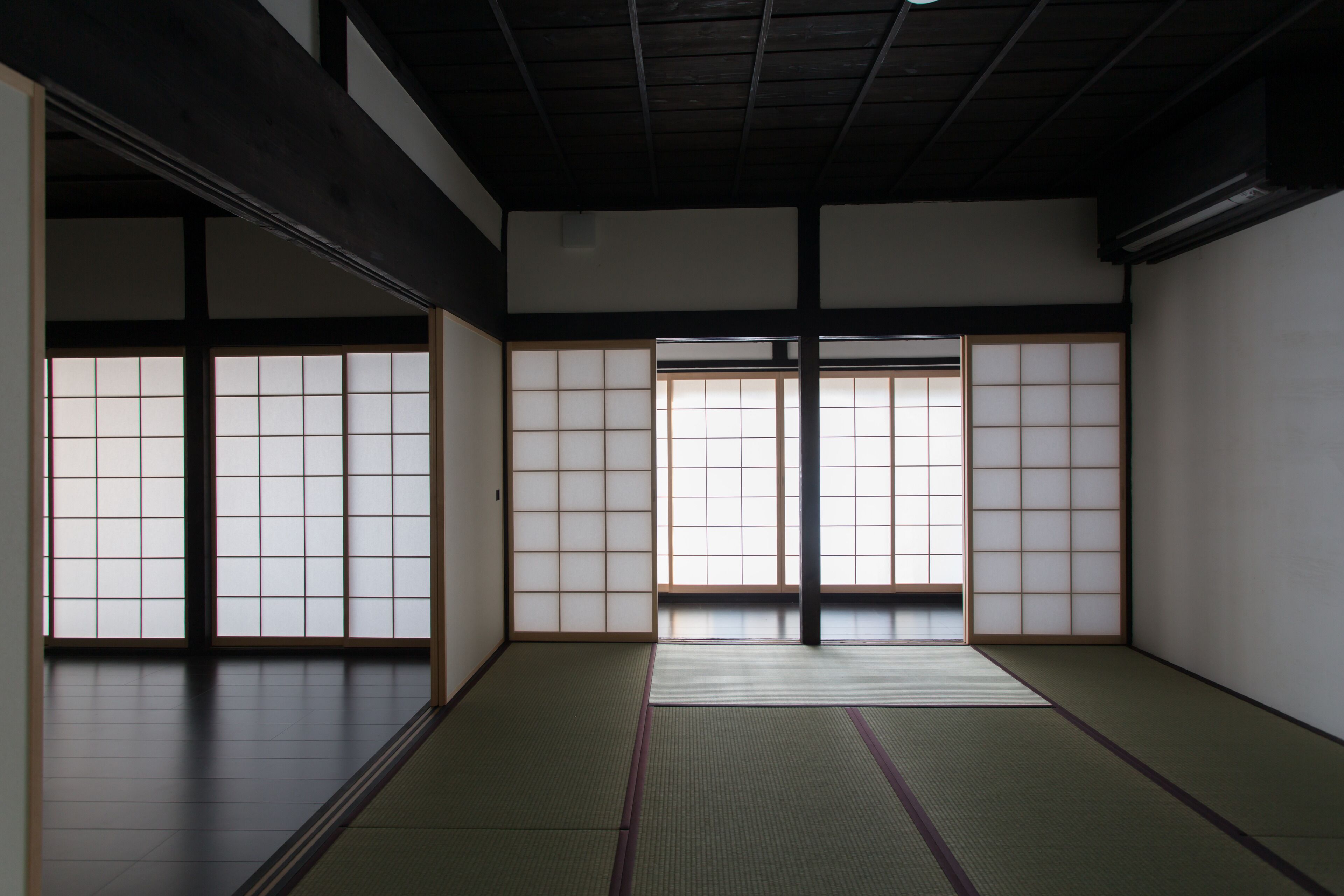 Una habitación tradicional japonesa con suelo de tatami, puertas correderas shoji y techo oscuro.