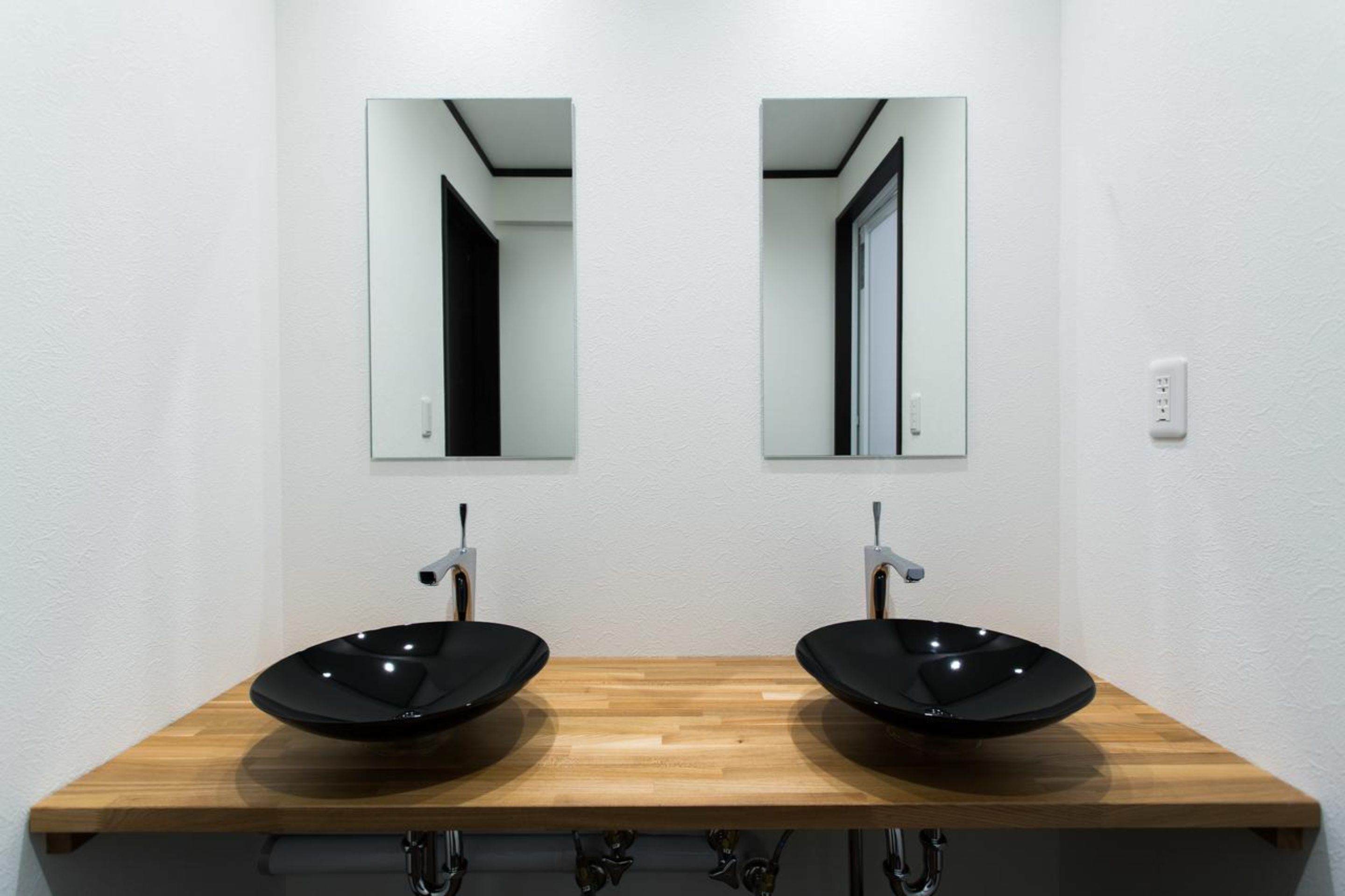 A bathroom with two black vessel sinks on a wooden countertop, flanked by mirrors on the wall.