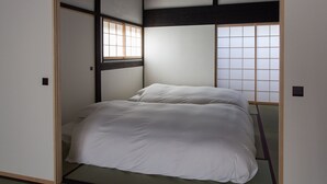 A traditional Japanese-style room with tatami flooring, a low bed with white bedding, and sliding shoji doors. - Solii (Ishikari)
