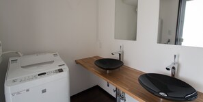 A compact bathroom with a washing machine, a wooden vanity with a black sink, and a mirror.