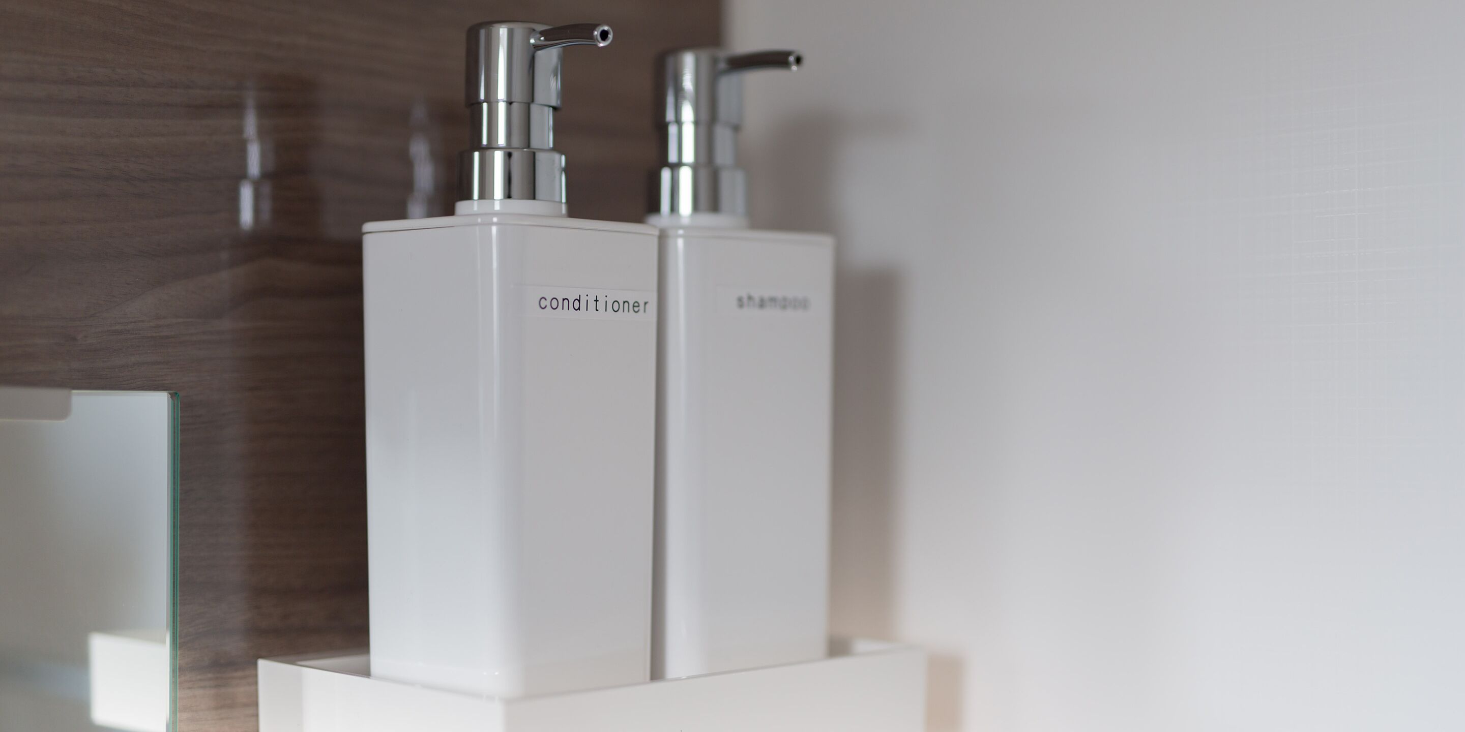 Two white bottles labeled 'conditioner' and 'shampoo' on a white shelf.
