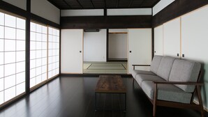 A traditional Japanese room with tatami flooring, a low wooden table, a sofa, sliding shoji doors, and a view of a tatami mat room. - Solii (Ishikari)