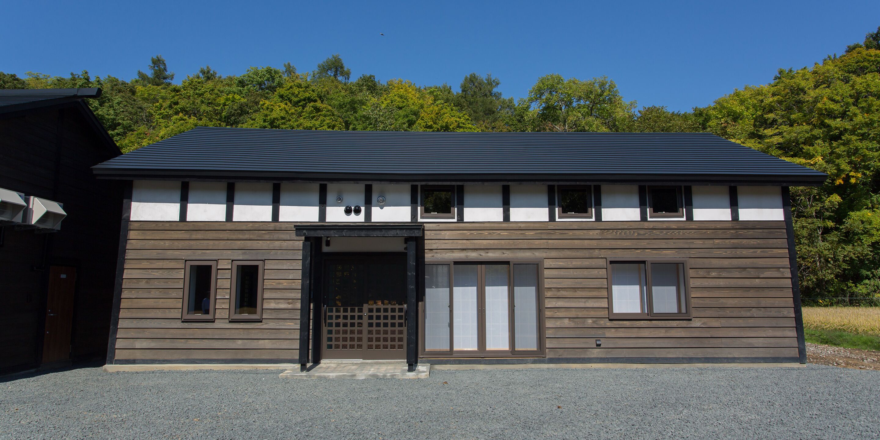 A modern building with a flat roof, a wooden facade, and a central entrance with a black door.