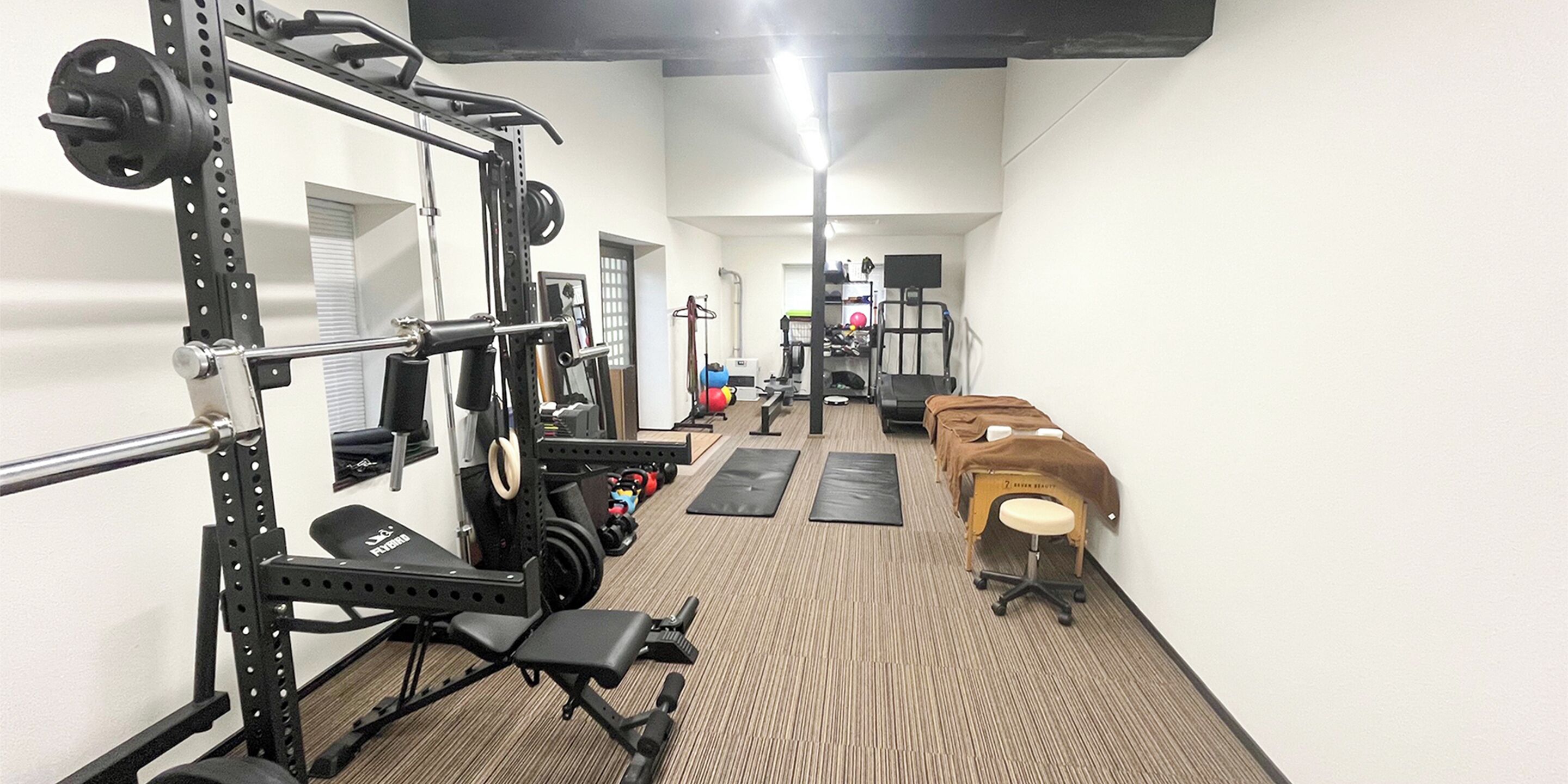 Un gimnasio con equipamiento de levantamiento de pesas, una banca y una mesa de masajes.