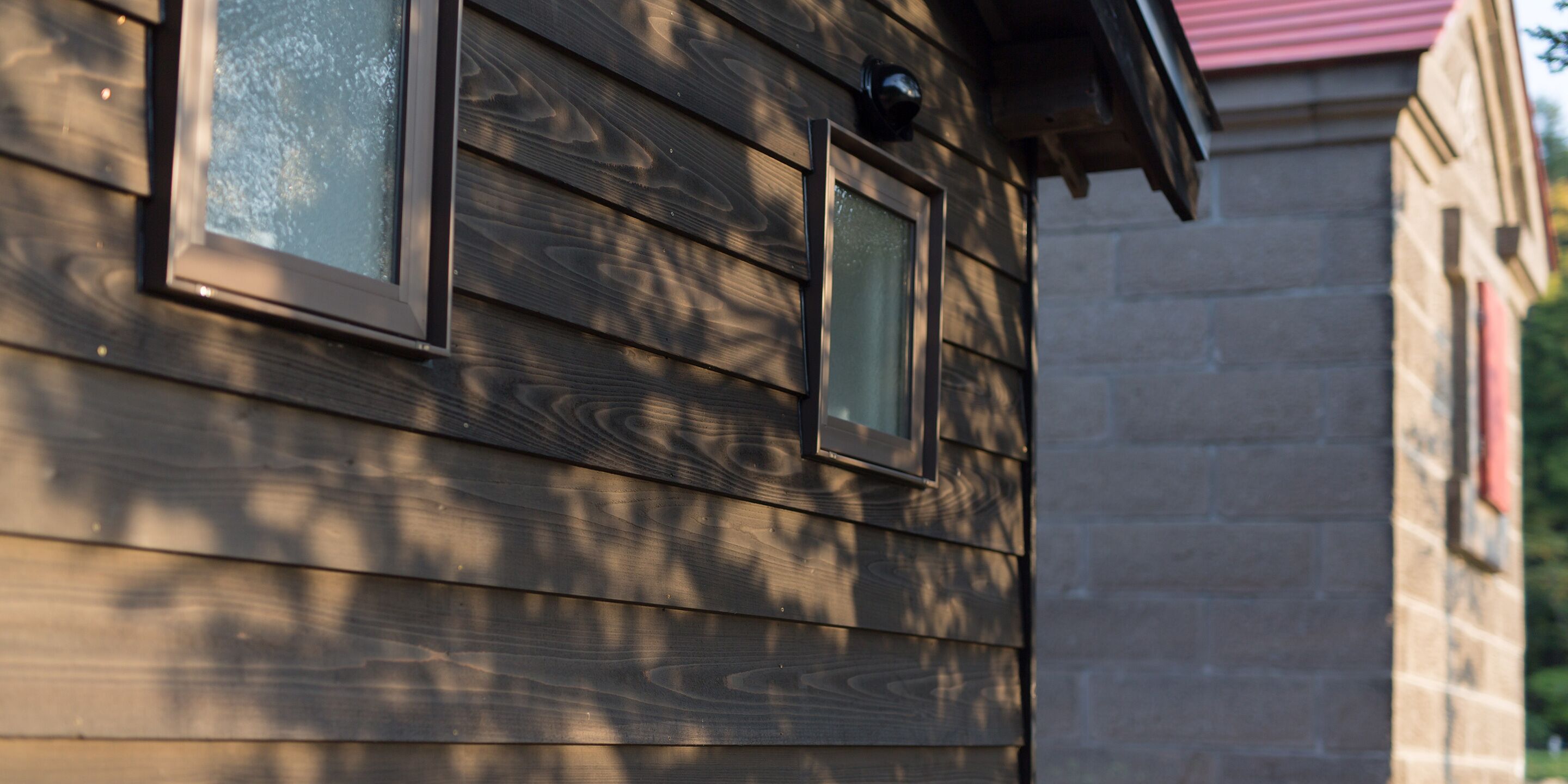 A wooden exterior wall with two windows and a small security camera.