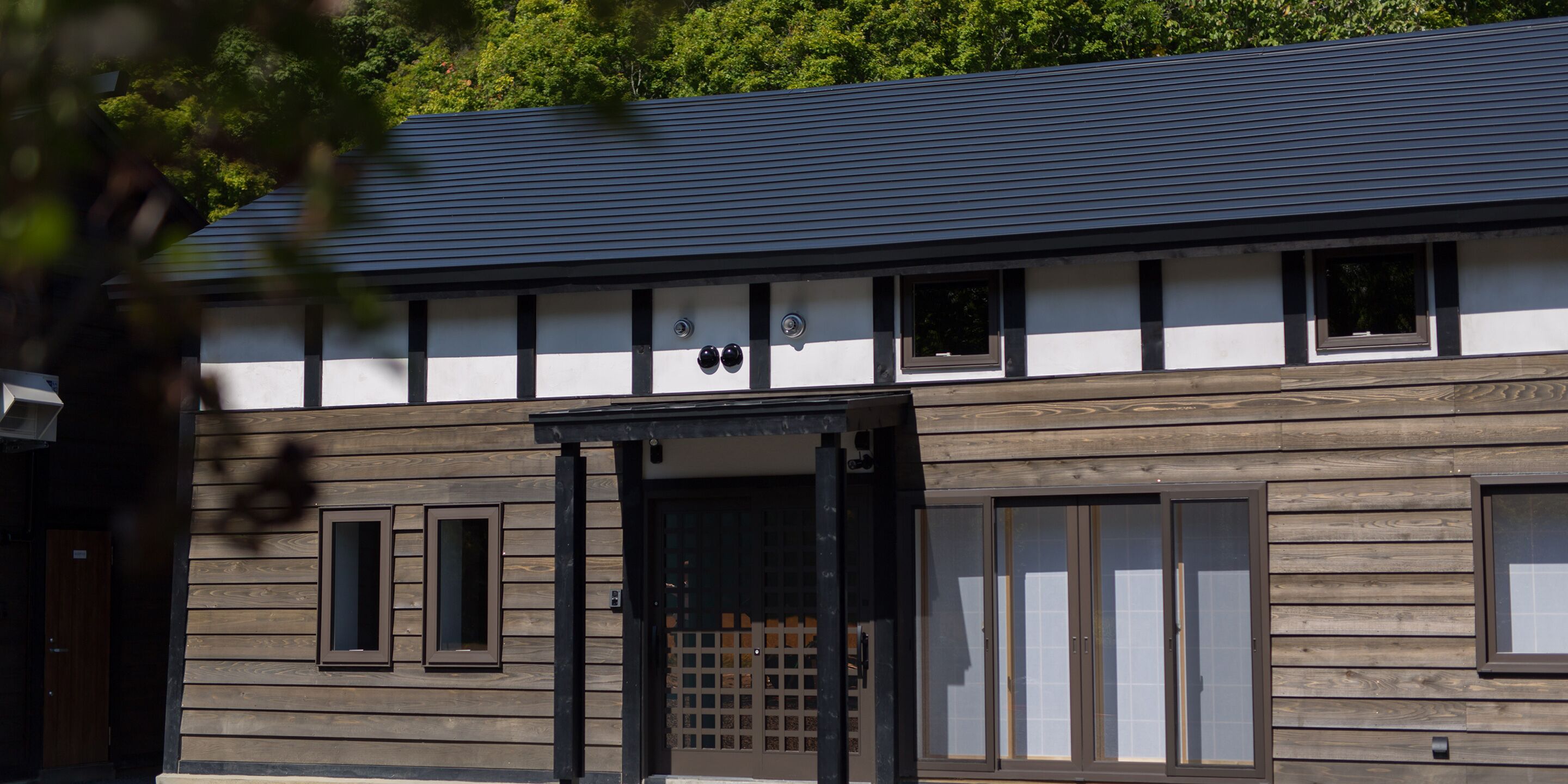 A building with a dark roof and white walls, featuring a wooden facade and a black-framed entrance.