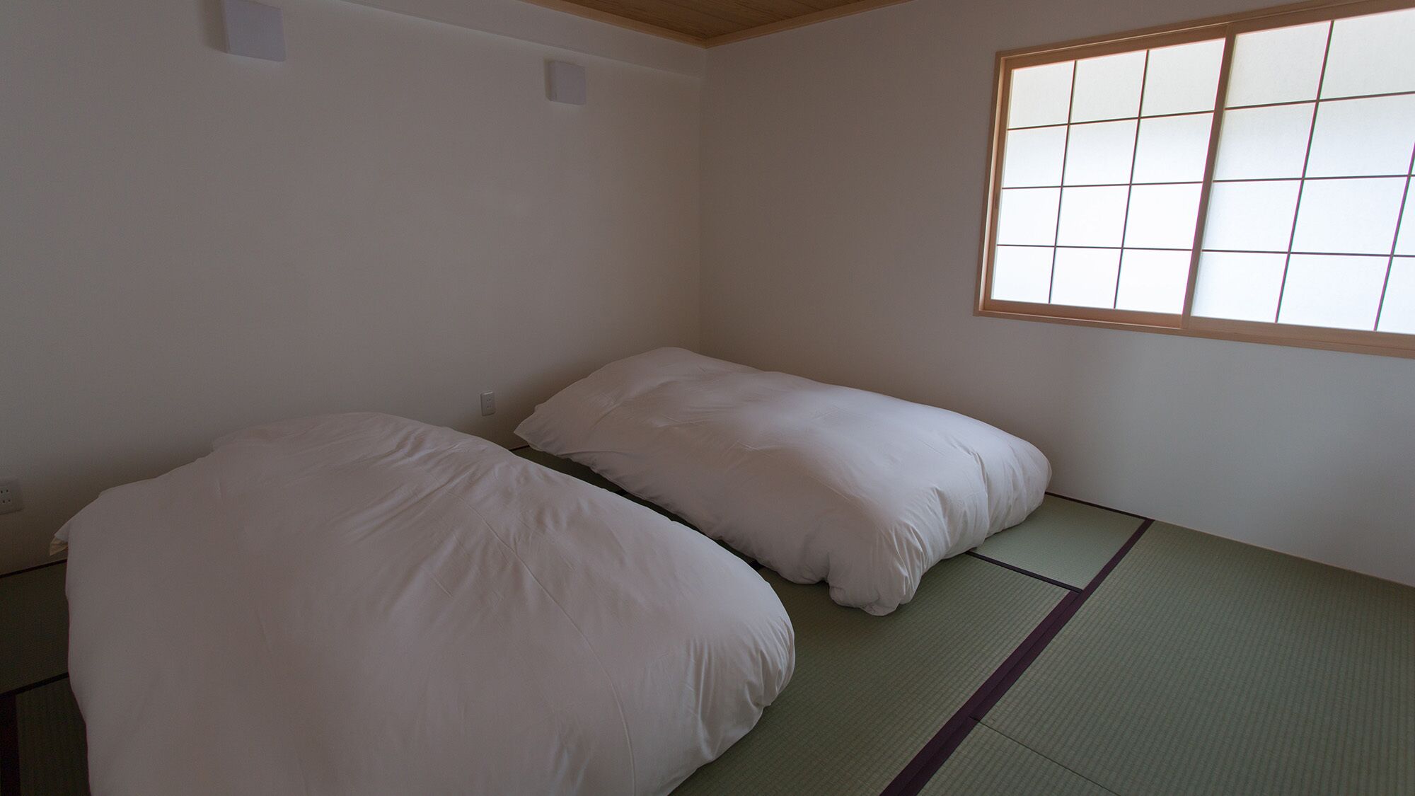 Una habitación con dos camas, una ventana con diseño de cuadrícula, esteras de tatami y techo de madera.