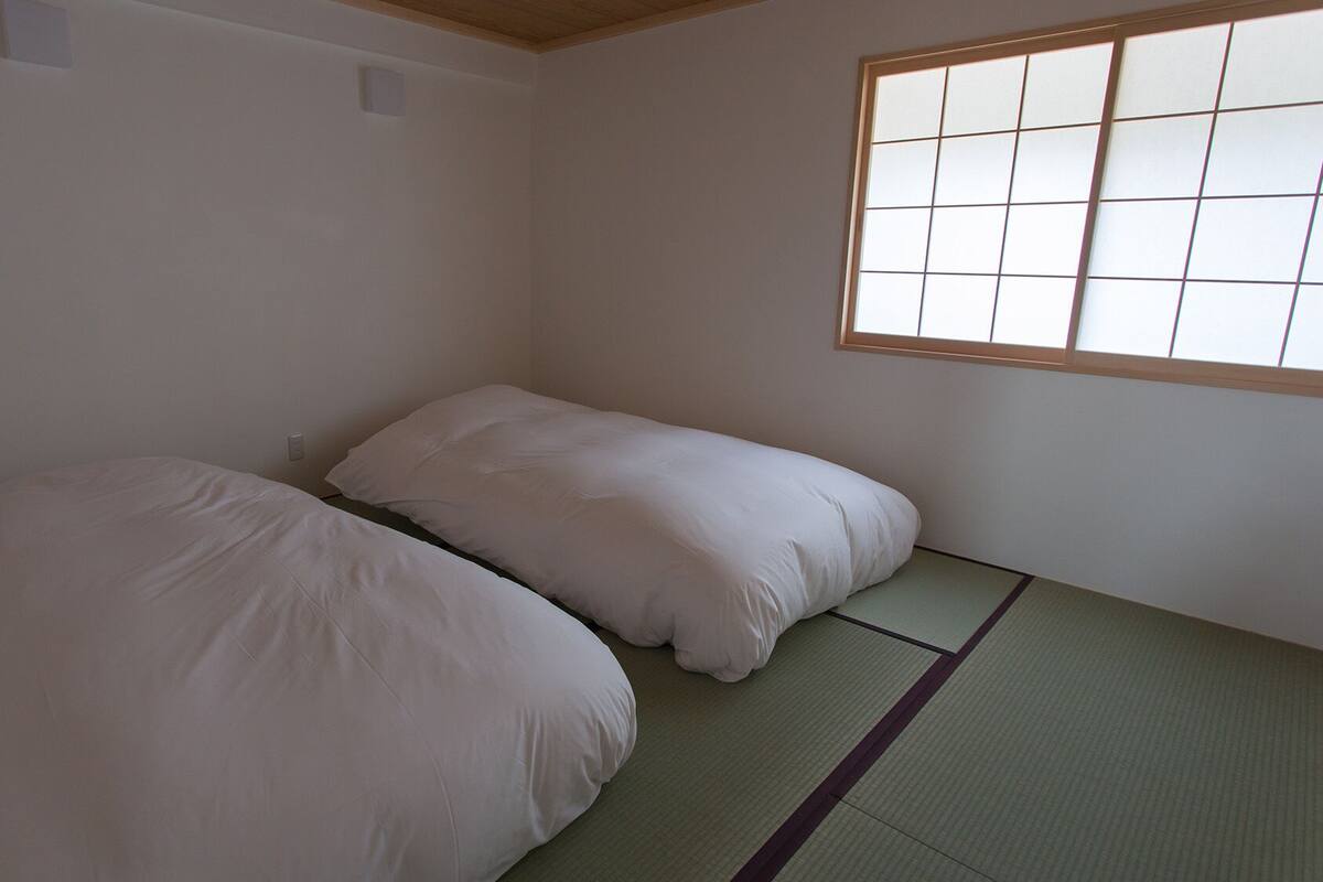 Una habitación con dos camas, una ventana con diseño de cuadrícula, esteras de tatami y techo de madera.