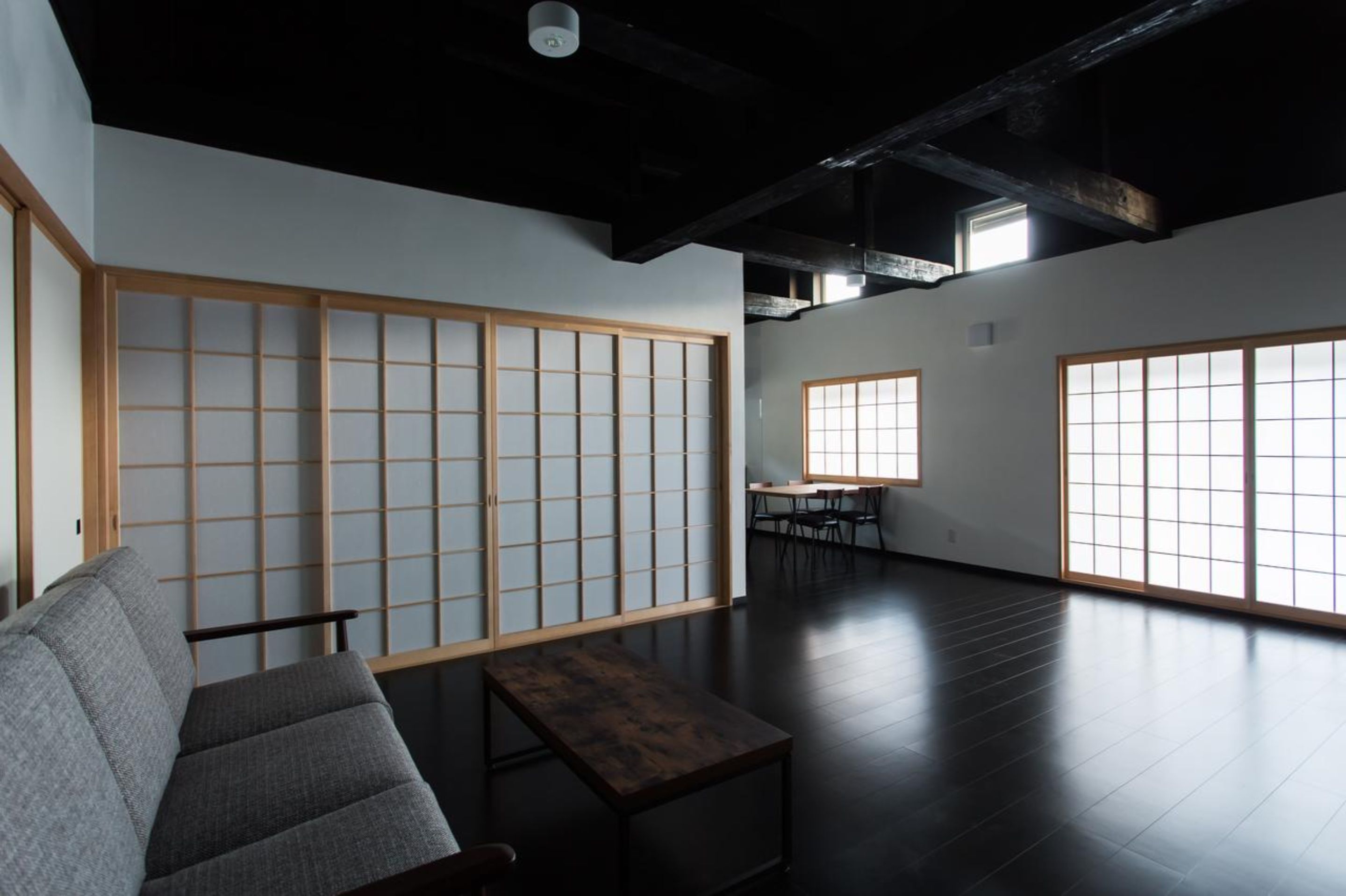 A modern interior with a tatami mat wall, a sofa, a table, and large windows.