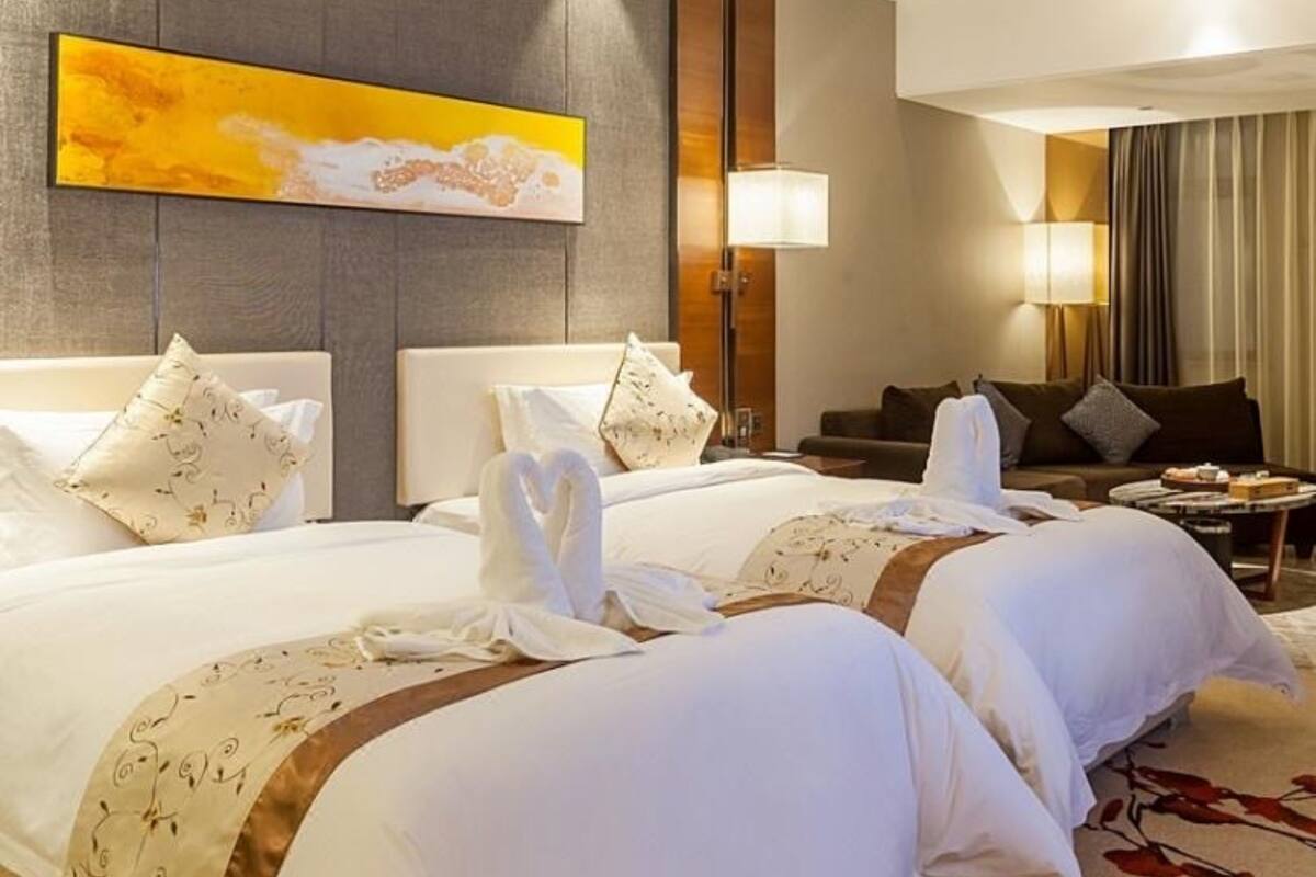 Habitación de hotel con dos camas, un cuadro abstracto grande, un sofá y una mesa de centro.