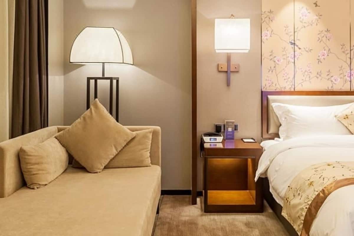 Habitación de hotel con sofá, mesita de noche con lámpara, escritorio pequeño con computadora y cama con cabecera floral.