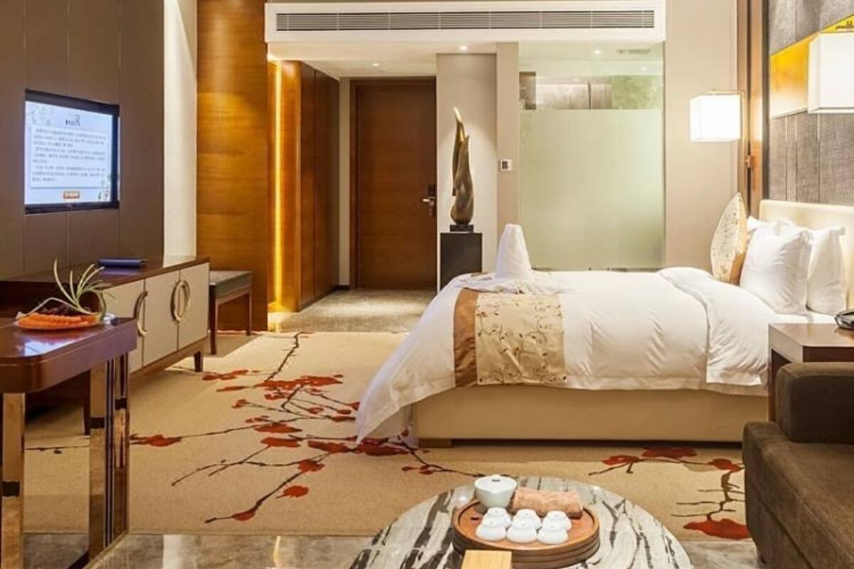 Habitación de hotel con cama, mesita de noche, televisión y un objeto decorativo en el suelo.