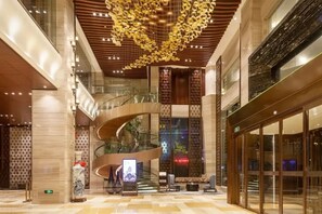 Un hall d’hôtel moderne avec un escalier en colimaçon, un grand lustre et un espace salon.