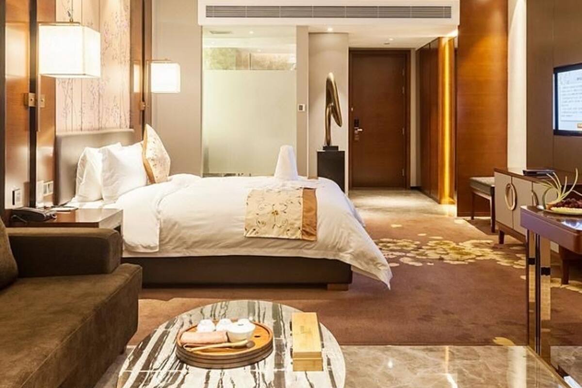 Habitación de hotel con una cama, un sofá, una mesa de centro, un televisor y una puerta que da a otra habitación.