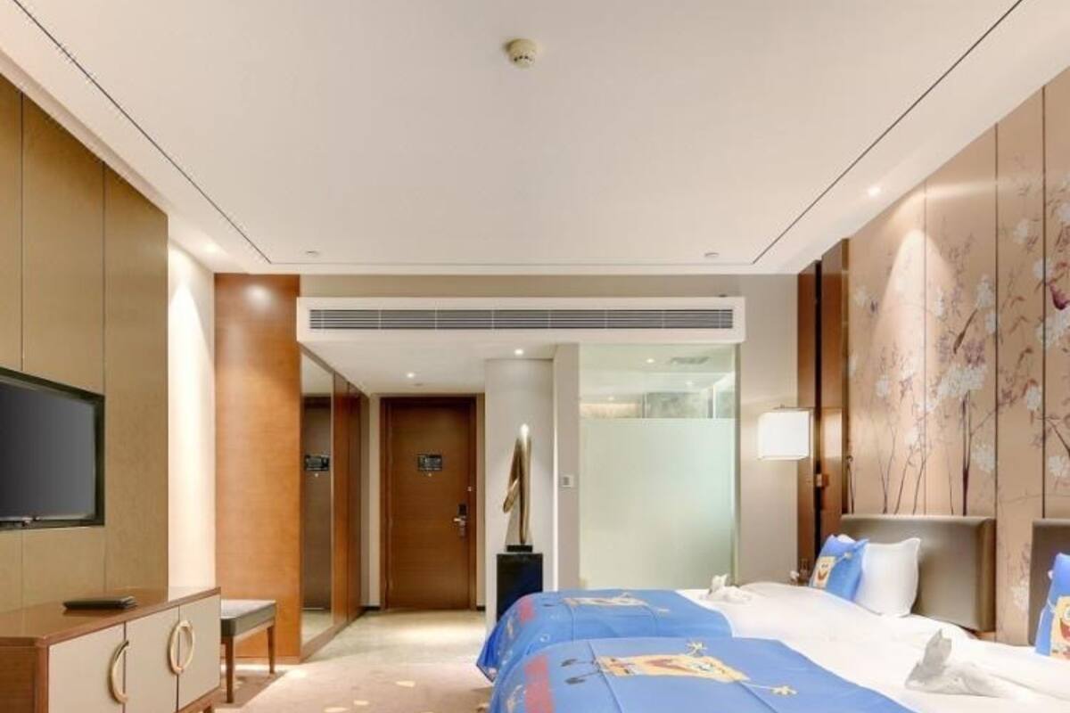Habitación de hotel con una cama grande, un televisor sobre un mueble, y un baño visible a través de una puerta abierta.