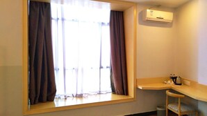 Une pièce dotée d’une grande fenêtre, d’un climatiseur intégré, d’une petite chaise en bois et d’un bureau d’angle avec une bouilloire et des tasses.