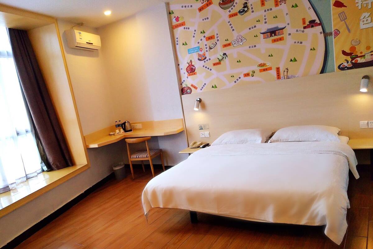 Een hotelkamer met een bed, een bureau met stoel, een raam met gordijnen en een wereldkaart aan de muur.