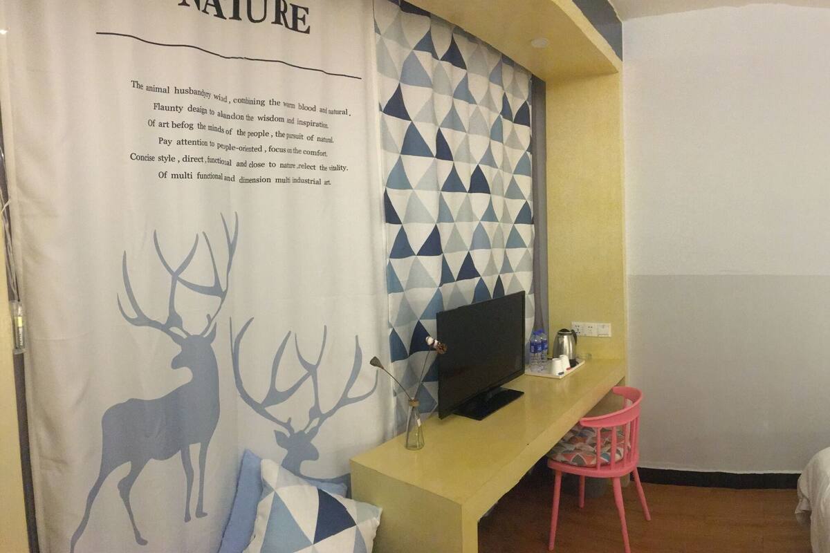 Hotelkamer met een bed, bureau met televisie, stoel en een muur met foto’s en een klok.