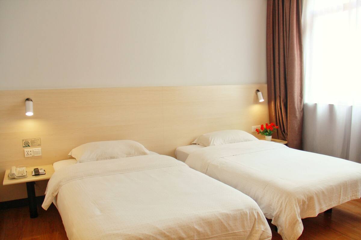 Een hotelkamer met twee bedden, een nachtkastje met een telefoon en een vaas met bloemen.