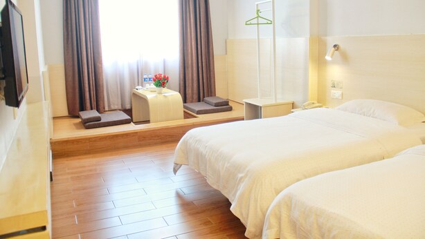 Une chambre d’hôtel avec deux lits, une table de chevet, une lampe, un miroir, une fenêtre avec des rideaux et un porte-manteau mural.
