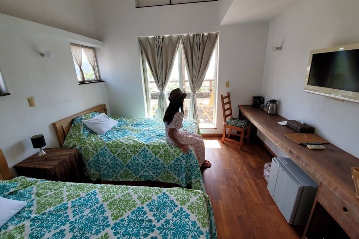 Ein Schlafzimmer mit zwei Betten, einem Schreibtisch, einem Fernseher und einem Fenster mit Vorhängen.